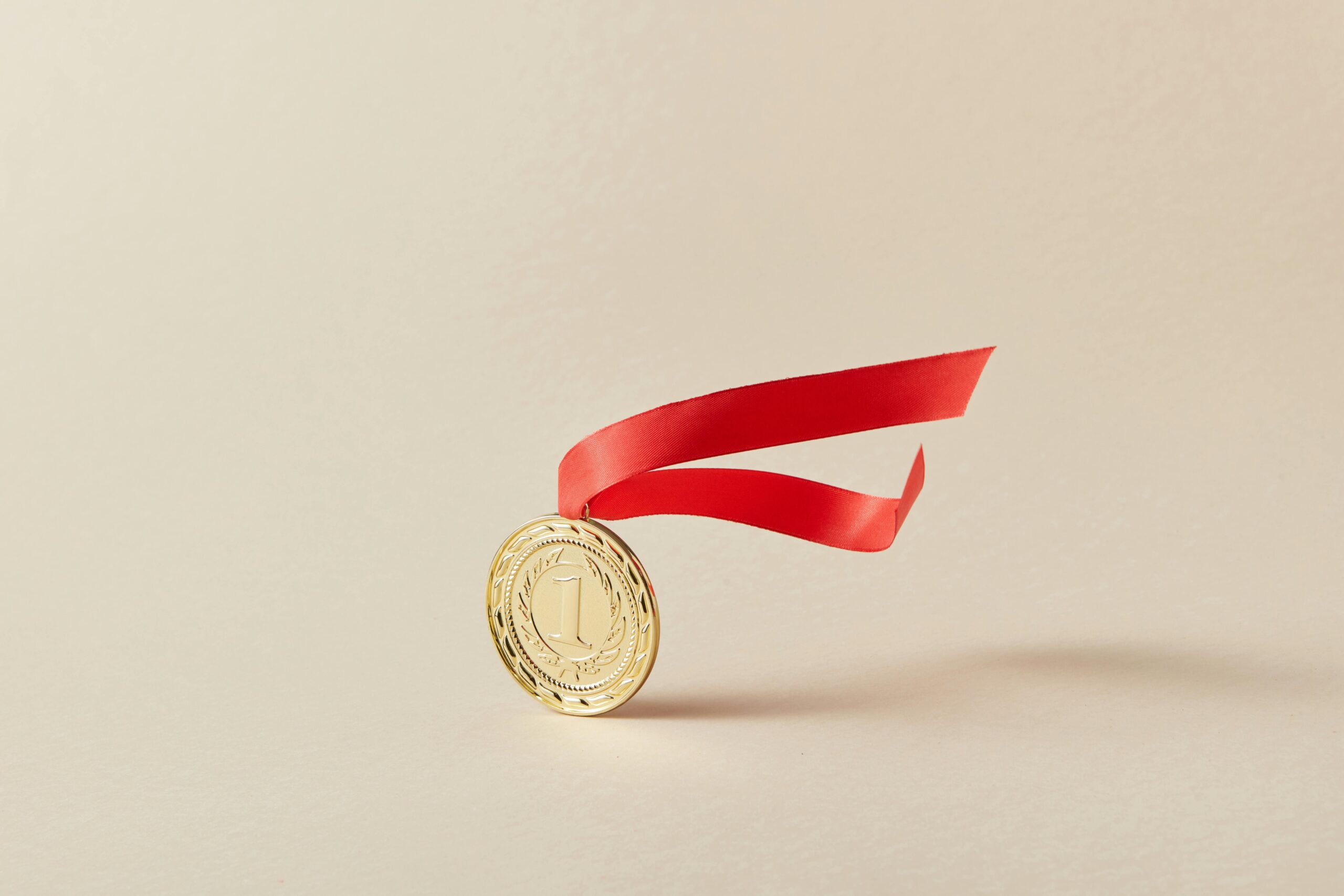 Close-up of a gold medal with a red ribbon against a neutral background.